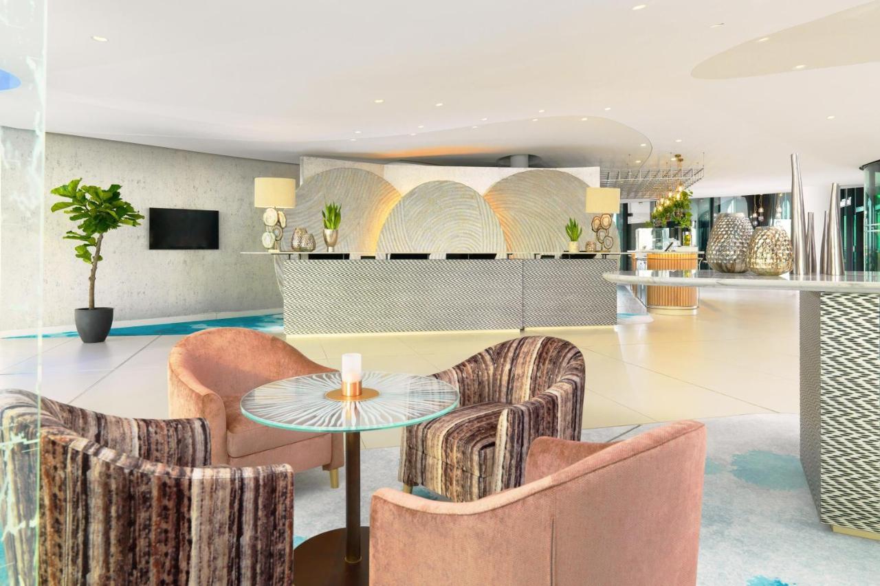 The Westin Hamburg Elbphilharmonie Hotell Eksteriør bilde The photo shows a modern hotel lobby with a stylish reception area. The reception desk has a sleek, contemporary design and is centered against a light-colored wall featuring abstract patterns. 

In front of the desk, there are two sets of seating ar