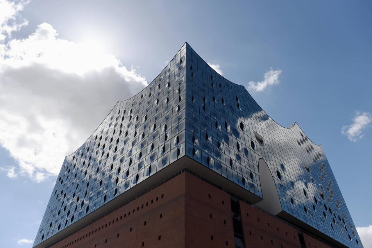 The Westin Hamburg Elbphilharmonie Hotell Eksteriør bilde The photo shows a modern architectural building characterized by a distinctive, wavy glass facade. The structure has a bluish tint with many large windows that reflect the sky and surrounding environment. The lower section of the building is made of 