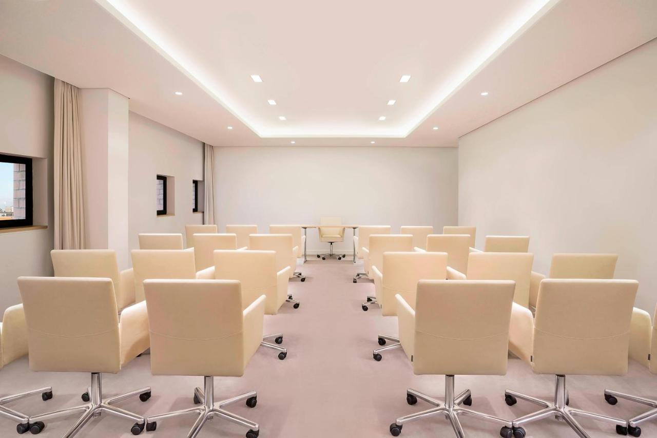 The Westin Hamburg Elbphilharmonie Hotell Eksteriør bilde The photo shows a modern conference room. There are several light-colored, wheeled chairs arranged in rows facing a central area where a glass table is located. The room has soft lighting from recessed ceiling lights, and the walls are mostly white, 