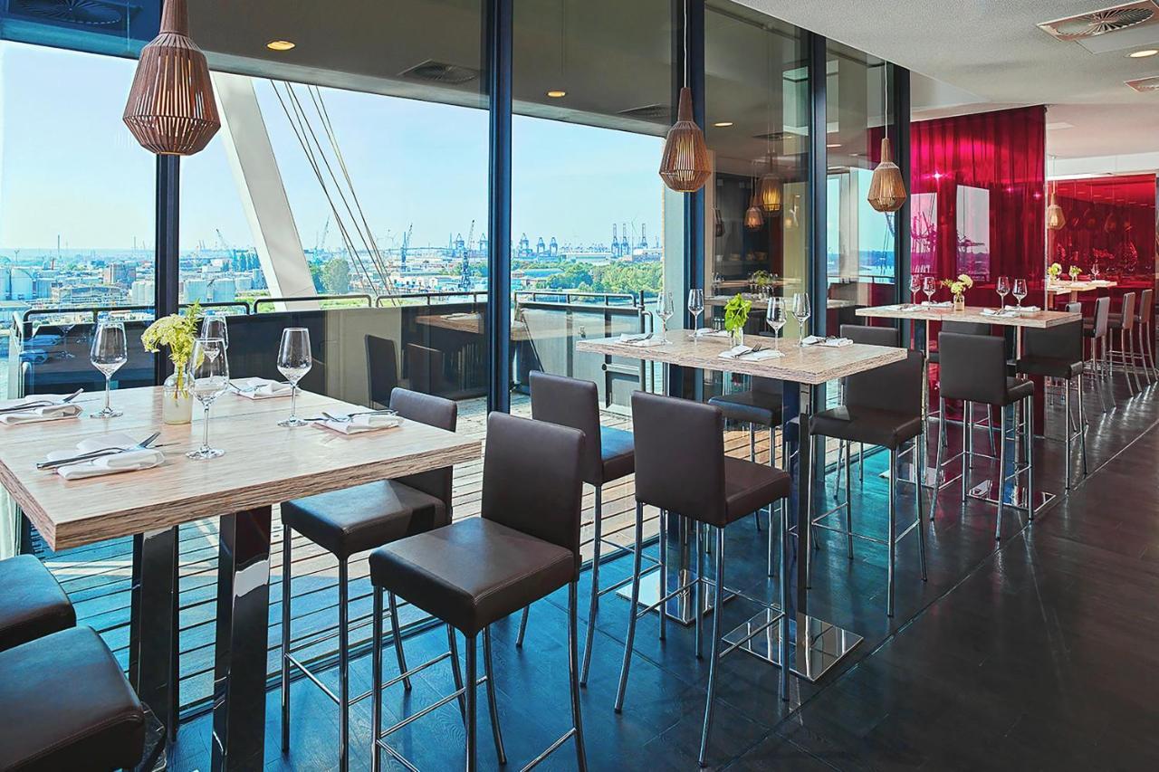 The Westin Hamburg Elbphilharmonie Hotell Eksteriør bilde The photo depicts a modern restaurant interior featuring a spacious dining area with large windows that provide a view of the outside. There are several tall tables with a light-colored surface and metallic bases, accompanied by dark, sleek stools. T