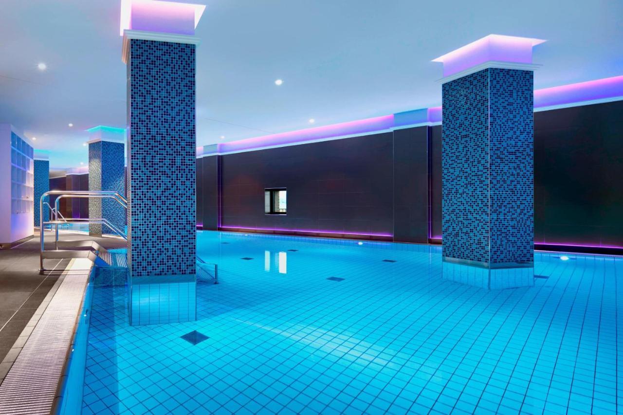 The Westin Hamburg Elbphilharmonie Hotell Eksteriør bilde The image shows a swimming pool area that features a modern, upscale design. The pool has bright blue tiles reflecting the water, creating a vibrant atmosphere. There are two columns dressed in a similar blue tile pattern, and the walls are adorned w