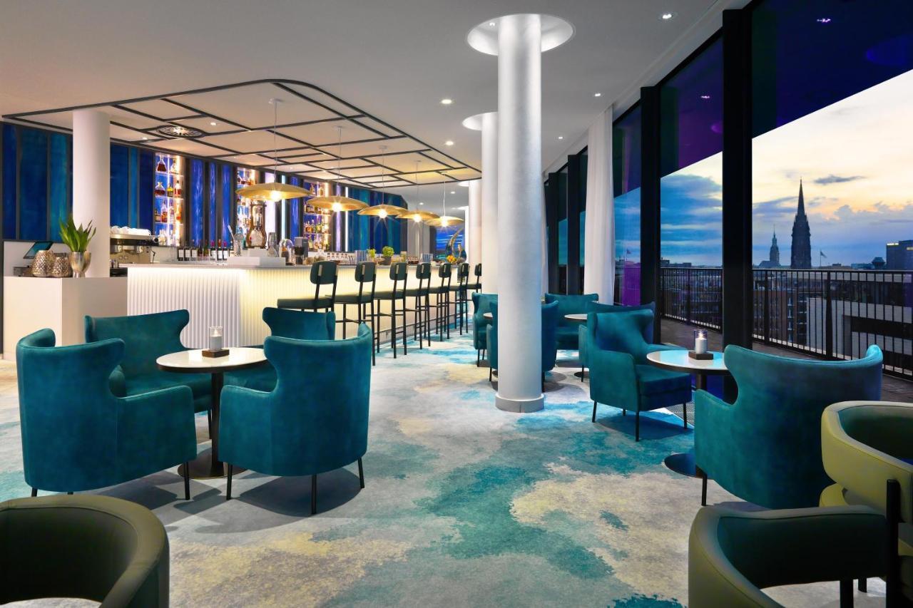 The Westin Hamburg Elbphilharmonie Hotell Eksteriør bilde The photo shows a modern lounge or bar area with a stylish design. It features plush turquoise chairs and small tables arranged around the space. In the background, there's a long bar with seating, illuminated by soft lighting. Large windows provide 