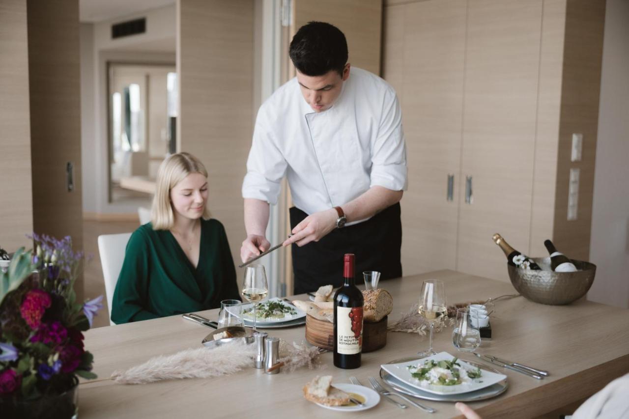The Westin Hamburg Elbphilharmonie Hotell Eksteriør bilde The photo depicts a dining scene in a modern setting. A man, dressed in a chef's attire, is serving food to a woman seated at the table. The woman is wearing a green outfit and appears to be enjoying the meal. The table is elegantly set with plates o