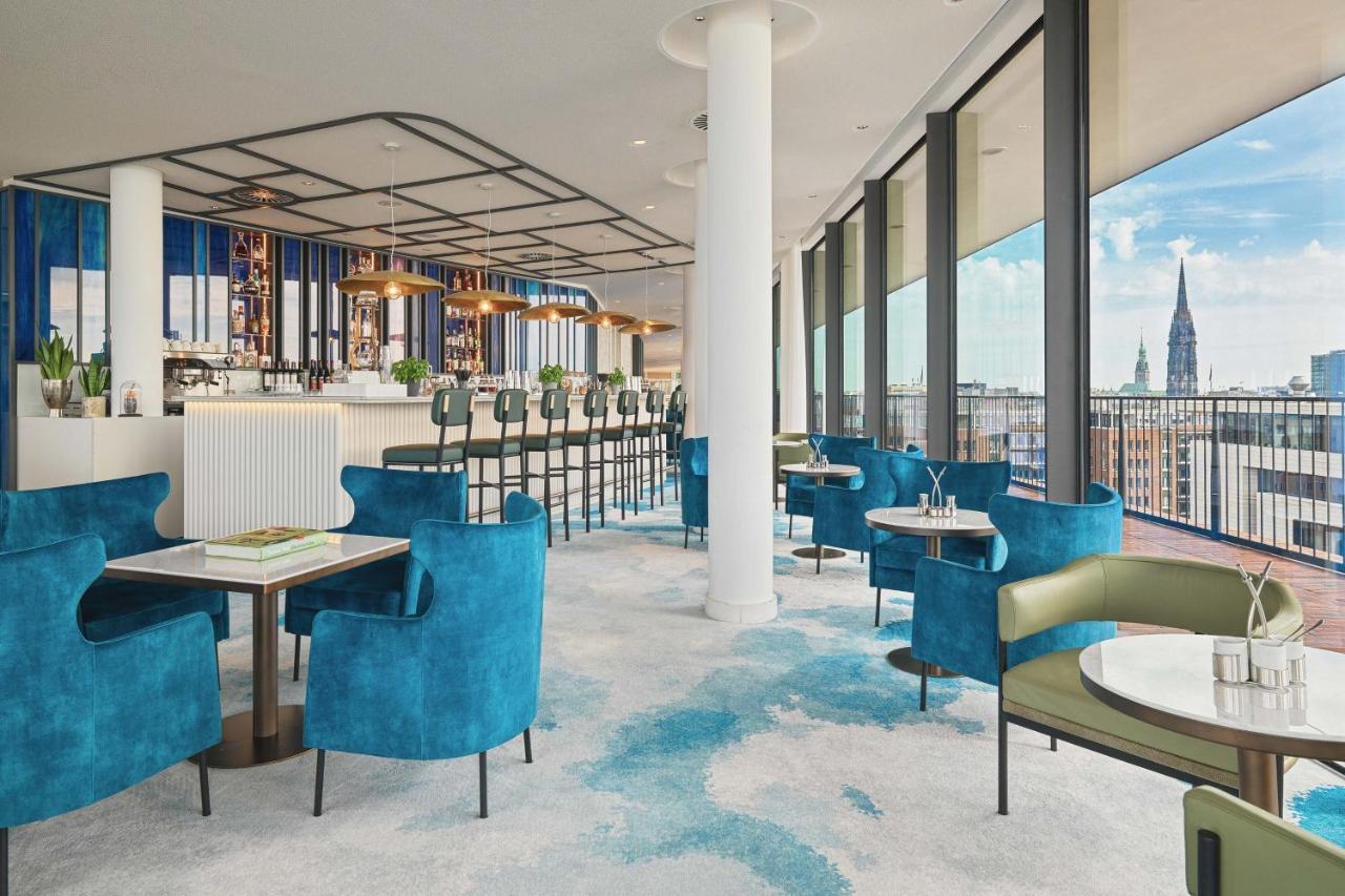 The Westin Hamburg Elbphilharmonie Hotell Eksteriør bilde The image shows a stylish and modern restaurant interior. There are several tables with blue and green chairs, creating a cozy atmosphere. The flooring features a light carpet with abstract patterns. Large windows provide plenty of natural light and 