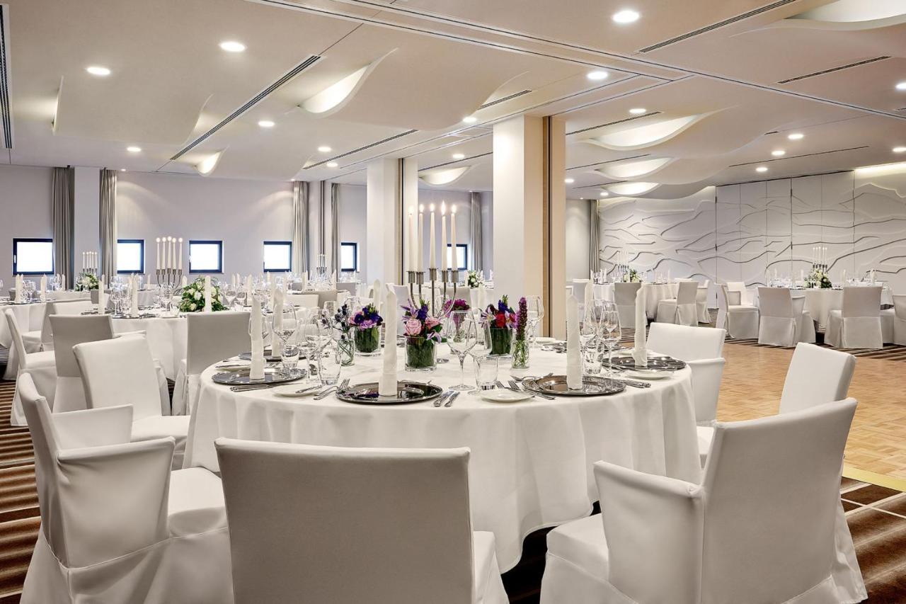 The Westin Hamburg Elbphilharmonie Hotell Eksteriør bilde The photo depicts a modern banquet or event hall setup. It features round tables covered with white tablecloths, each set with elegant dishware and glassware. The tables are adorned with floral centerpieces, adding a touch of color, and there are tal