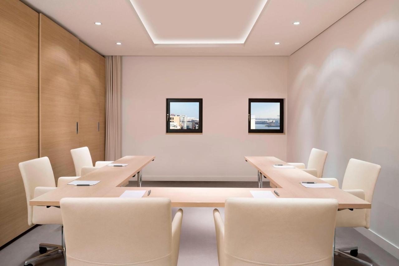 The Westin Hamburg Elbphilharmonie Hotell Eksteriør bilde The photo shows a modern conference room. It features a long, rectangular table made of light-colored wood, surrounded by several cream-colored chairs. The walls are painted in a light shade, and there are two framed windows on one wall that provide 