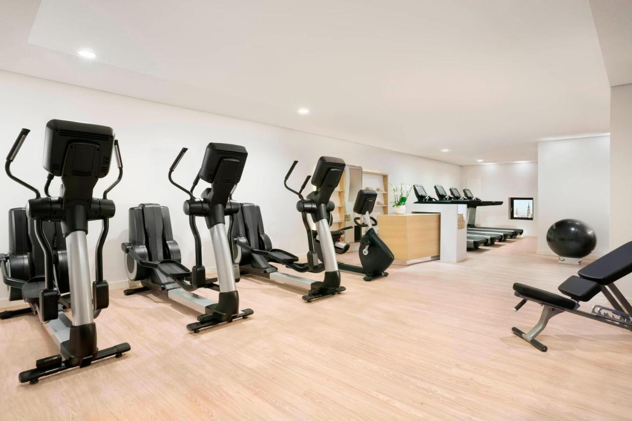 The Westin Hamburg Elbphilharmonie Hotell Eksteriør bilde The photo shows a fitness room with several pieces of exercise equipment. On the left side, there are multiple elliptical machines arranged in a row. In the center, there is a stationary bike. A workout bench is positioned nearby, and a large exercis