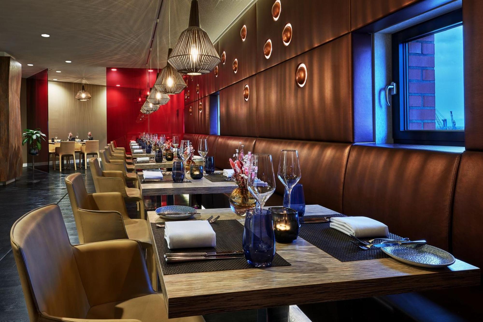 The Westin Hamburg Elbphilharmonie Hotell Eksteriør bilde The photo shows a modern restaurant interior. It features a series of wooden tables set for dining, each equipped with white napkins and utensils. The seating consists of comfortable leather chairs. The walls are decorated with a combination of warm 